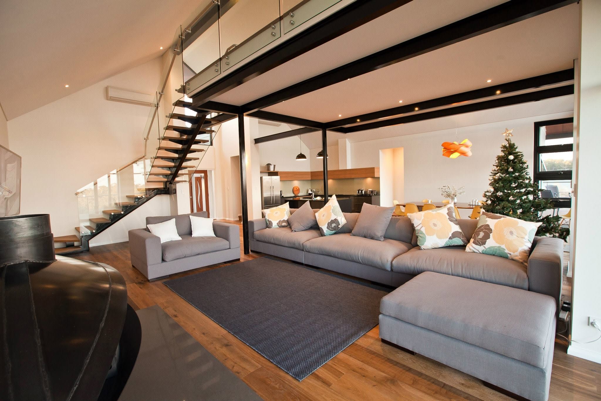 Open-plan lounge beneath a mezzanine, with exposed black steel beams and a suspended fireplace