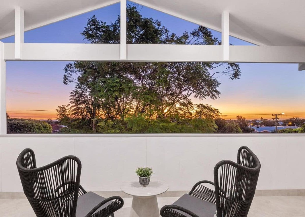 Upper-storey balcony framed by a white gable, looking out over treetops at sunset